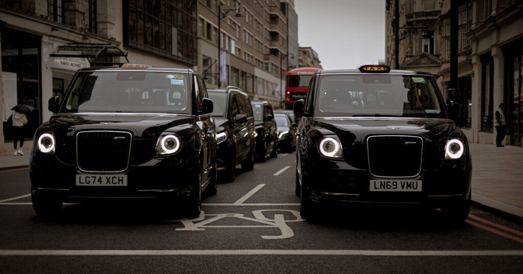 A row of black taxis parked along a busy city street, showcasing urban transportation.