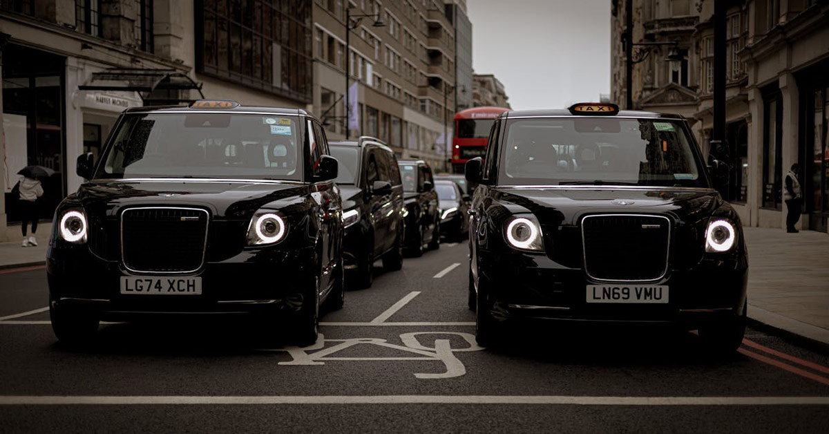 A row of black taxis parked along a busy city street, showcasing urban transportation.