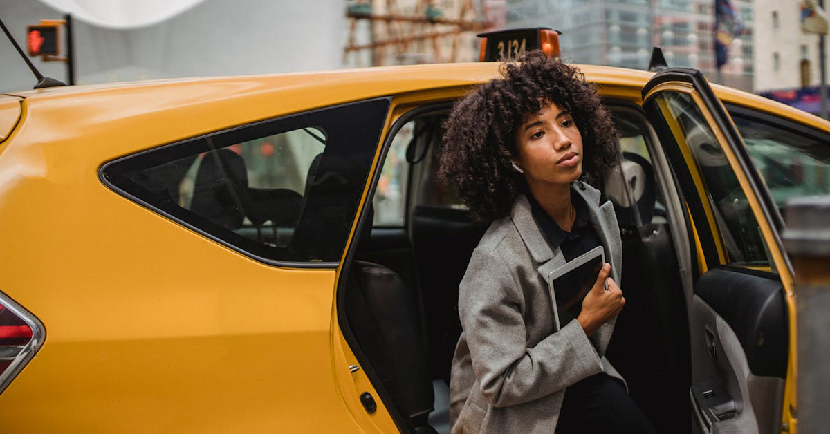 A woman getting out of a cab after when she reached her drop-off destination.
