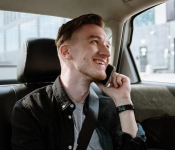 A man in the back seat of an airport taxi is talking on a cell phone, highlighting the convenience of pre-booking airport taxis.